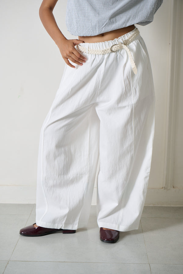 White wide-leg linen pants with an elastic waistband and a decorative cream drawstring, shown on a model wearing a light blue striped crop top and dark brown shoes.